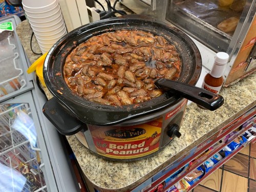 A slow cooker filled with boiled peanuts, sitting on a countertop in a convenience store.