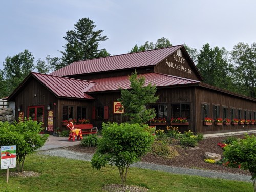 A rustic wooden building with a red metal roof, featuring flower boxes and a sign that reads "Polly's Pancake Parlor."