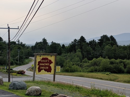 Sign for Polly's Pancake Parlor along a rural road, surrounded by trees and mountains in the background.
