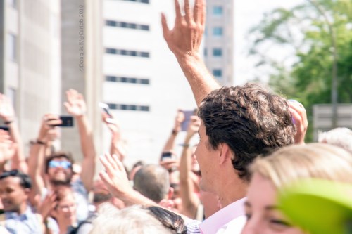 A crowd waves and takes photos, with a man in the foreground smiling and raising his hand.