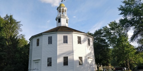 A round white building with a cupola, surrounded by trees and blue sky, showcasing a unique architectural design.
