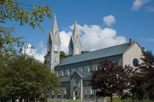 Historic stone church with twin spires, surrounded by trees and a blue sky with fluffy clouds.