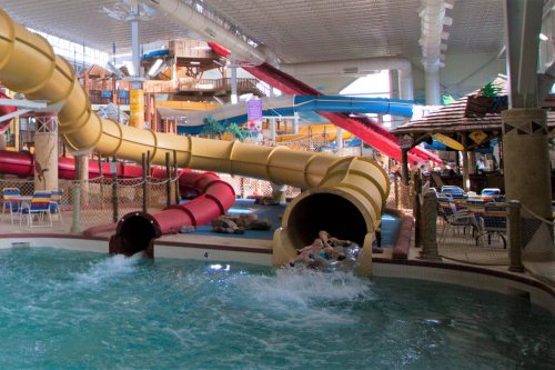 Indoor water park featuring colorful water slides and a pool with splashing water. Families enjoy the fun atmosphere.