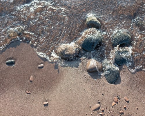 Waves gently lap at a sandy shore, revealing smooth stones partially submerged in the water.