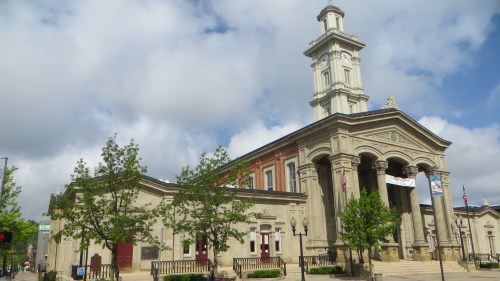 Historic building with a clock tower, surrounded by trees and a cloudy sky. Features classical architectural details.
