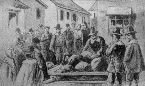 A historical scene depicting a crowd observing a grim event, with figures gathered around a cart in a village setting.