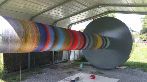 A large, colorful spool of thread inside a metal shelter, with vibrant layers of thread extending outward.
