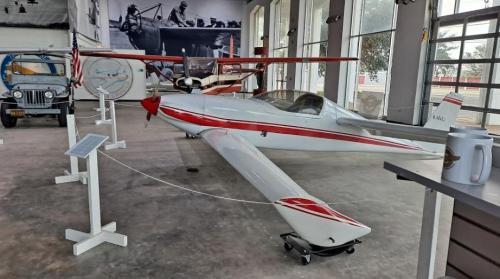 A sleek, red and white aircraft displayed in a museum alongside vintage vehicles and aviation memorabilia.