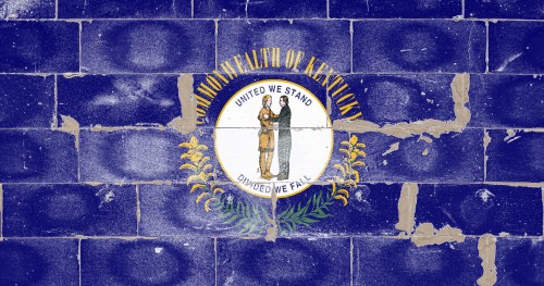 Kentucky state flag painted on a weathered blue brick wall, featuring the state seal and motto.