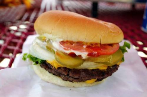 A juicy hamburger with lettuce, tomato, pickles, and cheese, served in a soft bun on a red picnic table.