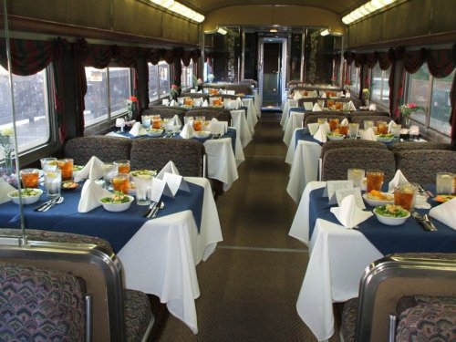 Elegant dining car with neatly set tables, white tablecloths, and floral centerpieces, ready for a meal.