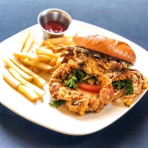 A crispy fried chicken sandwich with lettuce and tomato, served with fries and a small cup of ketchup.