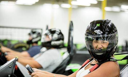 A group of people in go-karts wearing helmets, with one person smiling at the camera.