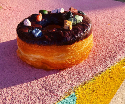 A glazed donut topped with colorful candy pieces, resting on a vibrant pink and yellow surface.