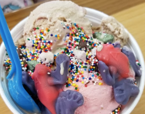 A colorful ice cream bowl topped with sprinkles and candy frogs in various colors.