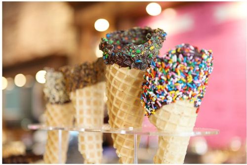 Colorful ice cream cones with chocolate and sprinkle toppings displayed in a shop.