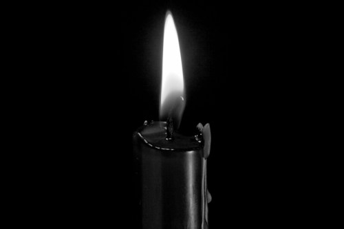 A close-up of a lit candle flame against a black background, casting a warm glow.
