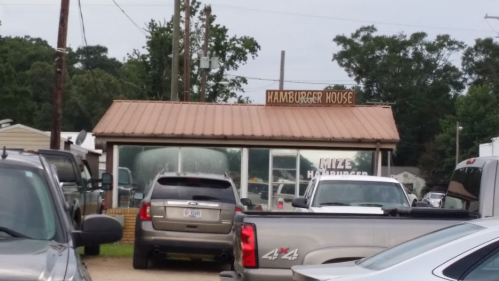 A restaurant called "Hamburger House" with a metal roof, surrounded by parked cars and trees in the background.