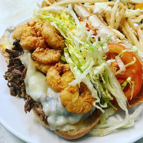 A hearty sandwich with pulled beef, shrimp, lettuce, tomato, and melted cheese, served with a side of fries.