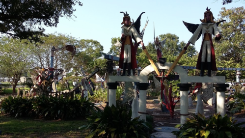 Colorful sculptures of angels and figures in a lush garden setting, surrounded by trees and greenery.