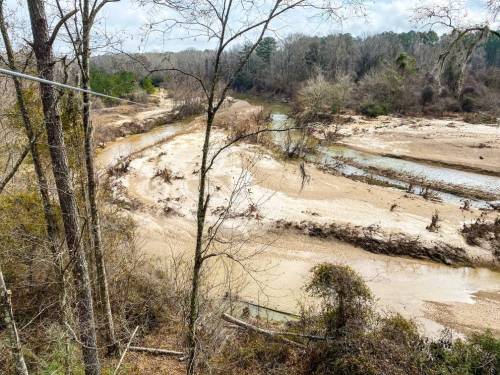 A winding river flows through a dry, sandy landscape surrounded by bare trees and sparse vegetation.