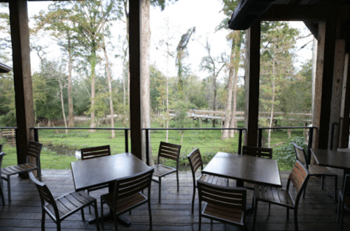 A wooden deck with empty tables and chairs overlooks a lush green landscape and trees.