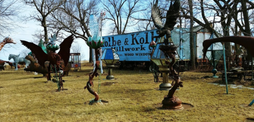 A sculpture garden featuring various metal art pieces and a truck in the background, set in a grassy area.