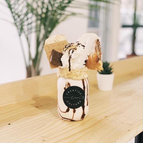 A tall milkshake topped with whipped cream, chocolate drizzle, graham crackers, and a chocolate bar in a jar.