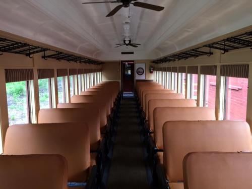 Interior of a vintage train car featuring rows of brown seats and large windows, with a view of greenery outside.