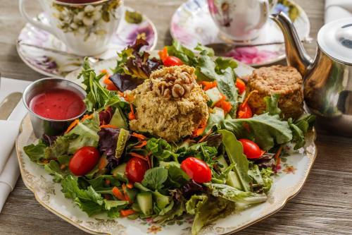 A colorful salad with mixed greens, cherry tomatoes, carrots, and a scoop of nutty salad, served with dressing and tea.