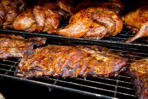 Close-up of grilled ribs and whole chickens on a barbecue grill, showcasing a smoky, flavorful appearance.
