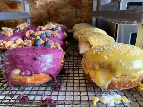 A display of colorful donuts: one with purple icing and blueberries, the other with yellow icing and sesame seeds.