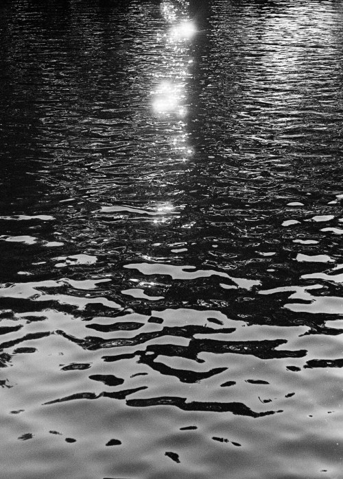 Black and white image of rippling water reflecting bright light spots.