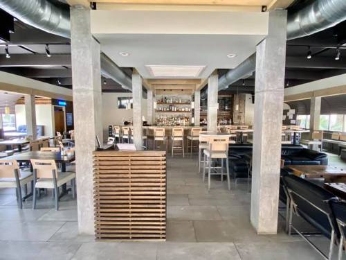 Modern restaurant interior featuring a bar, seating areas, and concrete pillars. Bright and spacious atmosphere.