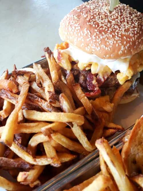A sesame seed burger topped with cheese and bacon, served with a side of crispy French fries.