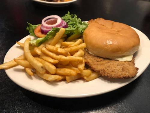 A plate with a crispy chicken sandwich, lettuce, tomato, onion, and a side of golden French fries.