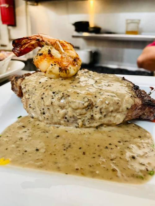 A juicy steak topped with a grilled shrimp and creamy pepper sauce, served on a white plate.