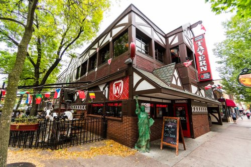 A charming tavern with a Tudor-style exterior, surrounded by trees and colorful flags, inviting patrons to enjoy drinks.
