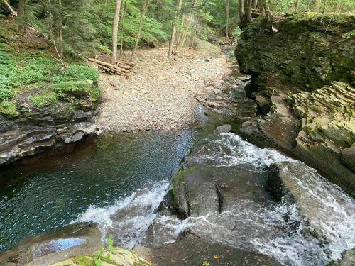 A serene river flows through a rocky landscape, surrounded by lush green trees and a pebbled riverbed.