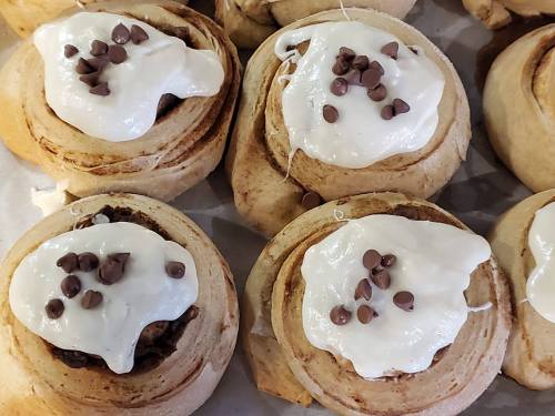 Freshly baked cinnamon rolls topped with cream cheese frosting and chocolate chips.