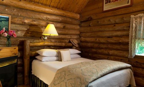 Cozy log cabin bedroom with a bed, decorative pillows, a lamp, and rustic wooden walls.