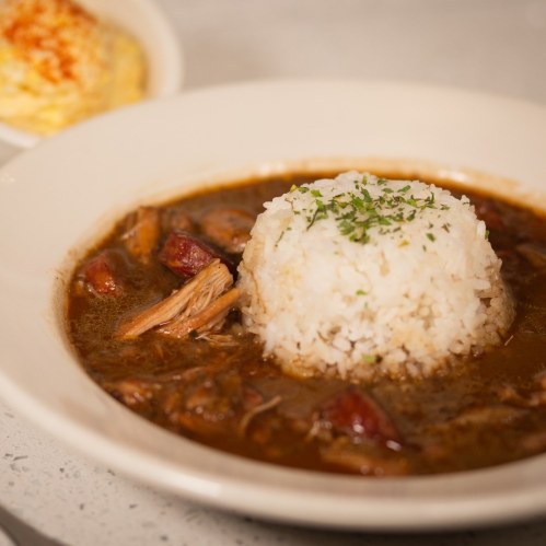 A bowl of rich stew with tender meat and a mound of white rice, garnished with parsley.