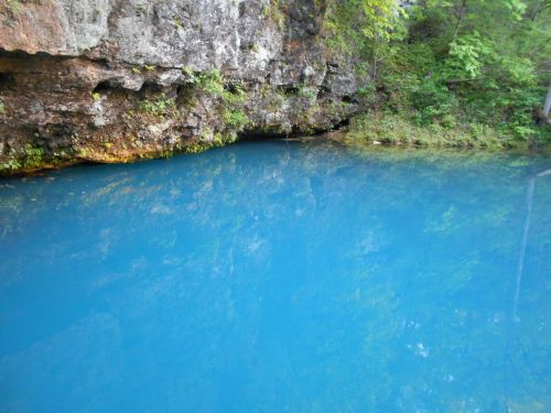 A serene blue pond surrounded by rocky cliffs and lush green foliage, reflecting the vibrant colors of nature.