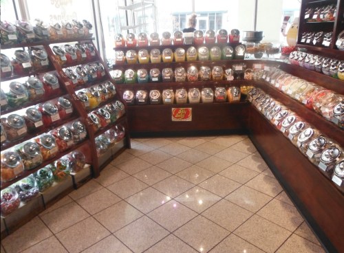 A colorful candy store display with jars of various candies on wooden shelves and a tiled floor.