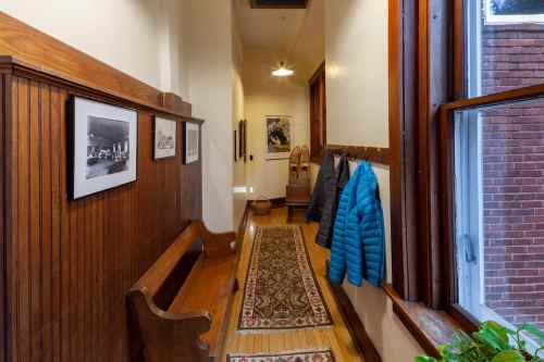 A narrow hallway with wooden walls, framed photos, a bench, a coat, and a patterned rug leading to a window.