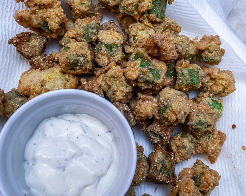 A plate of crispy fried okra pieces served with a small bowl of dipping sauce.