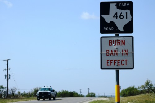A Texas road sign indicating Farm Road 461 and a burn ban in effect, with a truck driving in the background.