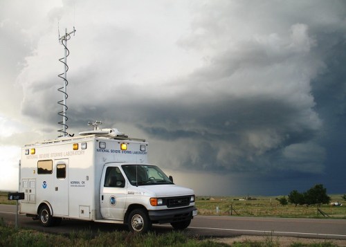 A storm chaser vehicle parked by the roadside, with dark storm clouds looming in the background.