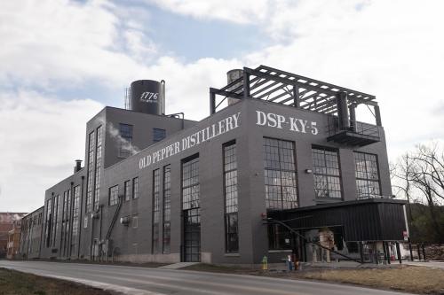 Old Pepper Distillery building with large windows and a water tower, set against a cloudy sky.