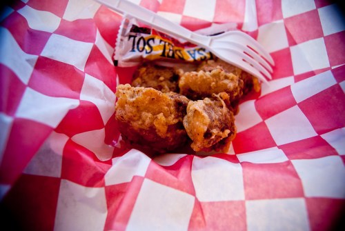 A basket lined with red and white checkered paper containing fried food and a plastic fork.